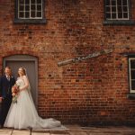 Bride and groom outside brick building, smiling.