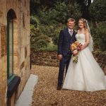 Smiling couple poses in wedding attire outdoors.