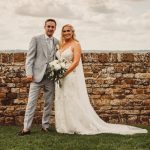 Bride and groom in front of stone wall.