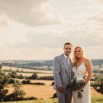 Couple in countryside, wedding attire, smiling.