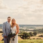 Couple in wedding attire with scenic countryside view.