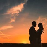 Silhouetted couple embracing at sunset background.