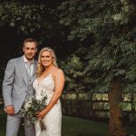 Bride and groom posing outdoors under tree.