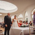 Wedding ceremony in sunlit room with guests seated.