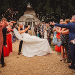 Happy couple kisses under confetti at outdoor wedding.