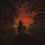 Couple embracing on bridge during sunset.