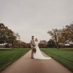 Wedding couple standing on tree-lined path.