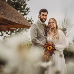 Bride and groom posing with bouquet outdoors.