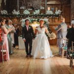 Bride and groom walking down aisle, guests applauding.