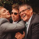 Three men laughing and hugging at a wedding.