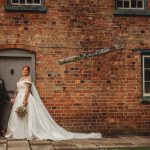 Bride and groom outside brick building, holding hands.