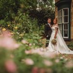 Couple in wedding attire by garden and house