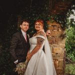 Wedding couple posing by ivy-covered stone archway.