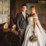 Bride and groom in rustic setting, wedding bouquet.