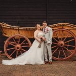 Bride and groom posing by rustic wooden cart.