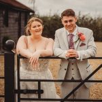 Bride and groom leaning on gate outdoors.