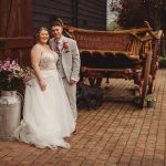 Bride and groom smiling beside vintage farm cart.