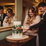 Couple cutting wedding cake together, smiling.