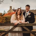 Couple smiling by wooden gate, autumn garden background.