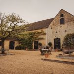 Rustic courtyard with stone building and tree.