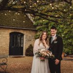 Bride and groom under garden lights, rustic setting.