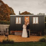 Couple posing outside cottage in autumn garden.