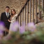 Couple on rustic stairs with purple flowers.