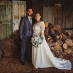 Bride and groom standing by stacked logs indoors.