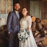 Bride and groom pose by chopped logs.