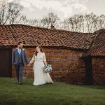 Couple walking by old brick building on wedding day.