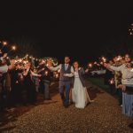 Newlyweds exit under sparklers at night celebration.