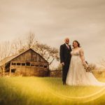 Bride and groom near rustic barn at sunset.