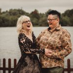 Two people laughing by a lakeside fence.