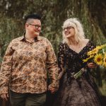 Couple laughing, holding hands, with a sunflower bouquet.