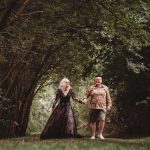 Couple holding hands walking through woodland path.