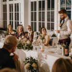 Man giving wedding speech at decorated dinner table.