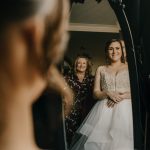 Bride and woman reflected in mirror, smiling.