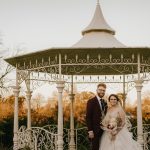 Bride and groom under decorative gazebo at sunset.