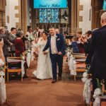 Bride and groom walking down church aisle smiling.