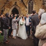 Happy couple exits church with wedding guests cheering.