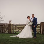 Smiling couple pose in countryside wedding photo.