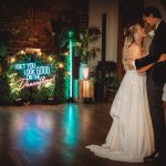 Bride and groom dancing with neon sign backdrop.