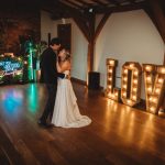 Couple dancing in front of illuminated love sign.