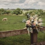 Rustic bouquet on wooden fence in countryside field.