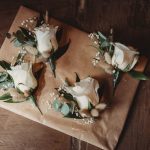 White rose boutonnieres on brown paper background.