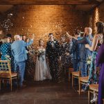 Bride and groom walking amidst confetti indoors.