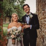 Bride and groom smiling with drinks and flowers.