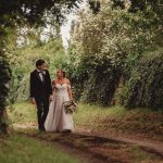 Bride and groom walking down a leafy path.