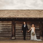 Bride and groom holding hands, rustic wooden backdrop.