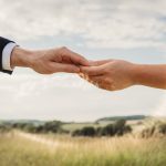 Couple holding hands in countryside landscape.